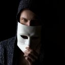 a person holding a white mask in front of their face as they are situation in a dark room.