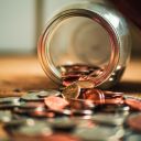 Jar full of Pennie’s that’s has tipped over spilling coins onto the surface.